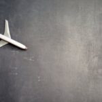 Art Tours - Top view of crop anonymous person driving toy airplane on empty blackboard while representing journey concept