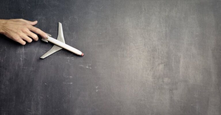 Art Tours - Top view of crop anonymous person driving toy airplane on empty blackboard while representing journey concept