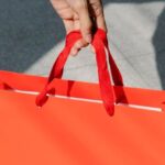 Holiday Markets - High angle of crop anonymous female buyer taking red paper bag with purchase in sunshine