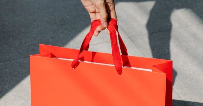 Holiday Markets - High angle of crop anonymous female buyer taking red paper bag with purchase in sunshine
