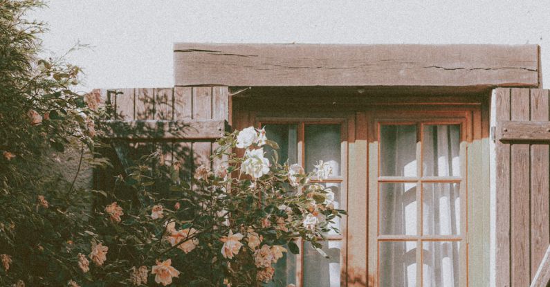 Neighborhoods - Exterior of cozy residential house with wooden window and tiled roof near lush blossoming tree on sunny day