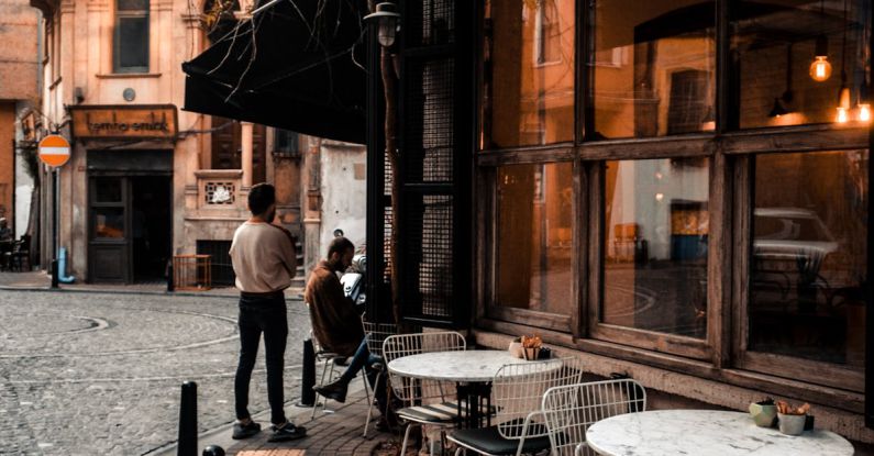Historic Districts - Facade of cafe with large windows and tables on sidewalk along road and faceless people resting in city